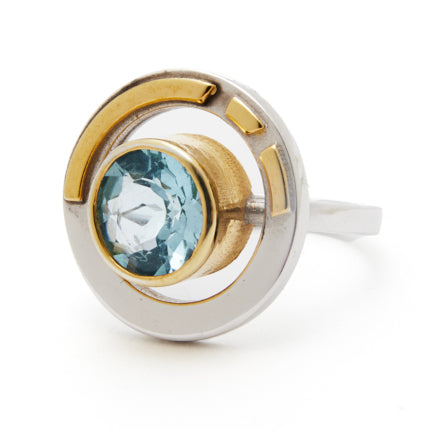 Introducing the Elodie Ring in Silver Gold & various gemstones by Gallardo & Blaine Designs: a modern piece featuring a circular design and a central light blue gemstone set in gold. This ring also incorporates silver and gold details, effortlessly blending contemporary elegance with vintage style glamour.