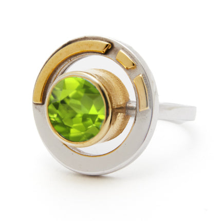 The Elodie Ring in Silver Gold & various gemstones by Gallardo & Blaine Designs is a perfect blend of vintage style glamour and modern design, featuring a bright green gemstone set in the center of a round, two-toned band. The primarily silver band with gold accents creates a contemporary geometric look, while the faceted cut of the gemstone enhances its vibrant color.