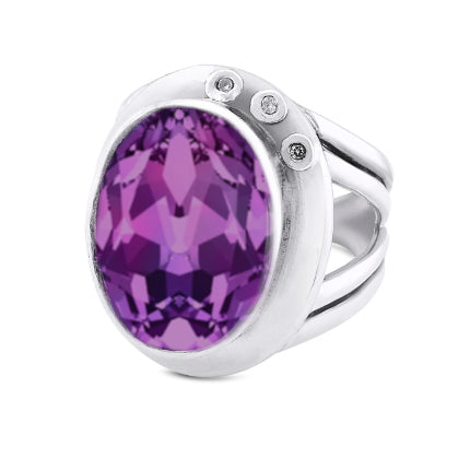 The Eyetelia Ring in various gemstones by Gallardo & Blaine Designs features a large, faceted oval purple gemstone set in the center. This silver statement cocktail ring boasts a modern design with a split shank and three small round diamonds embedded in the metal on one side of the setting, offering an adjustable design for a perfect fit.