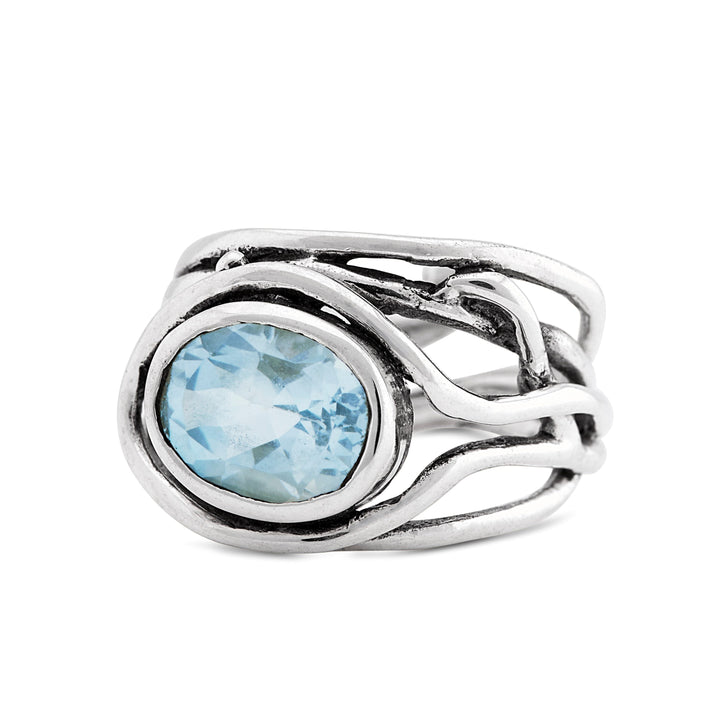 A Fossil Ring in silver & various gemstones by Gallardo & Blaine Designs with an intricate, intertwined band design featuring a large, oval-shaped, light blue gemstone at its center. The band twists around the gemstone in a unique, artistic fashion, making this adjustable ring both beautiful and versatile.