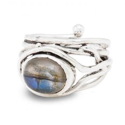 A Fossil Ring in silver & various gemstones featuring an oval labradorite gemstone with iridescent blue and grey hues by Gallardo & Blaine Designs. The band has a twisted, organic design with an additional small silver ball detail. This adjustable, handcrafted gemstone ring boasts a rustic charm.