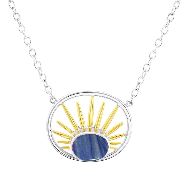 The Gallardo & Blaine Designs Goddess Necklace Small in various gemstones showcases a silver chain featuring a pendant with a circle design. The sterling silver pendant displays a central blue stone, surrounded by gold and silver rays extending outward, resembling a stylized sun. The chain is simple with evenly spaced links.