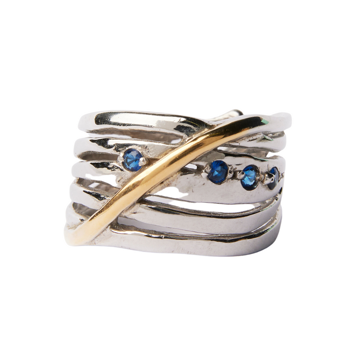 A chunky statement ring in sterling silver, featuring seven wavy, overlapping strands with a single gold accent crossing diagonally. This Hidden Gems Ring in Silver & Gold by Gallardo & Blaine Designs is adorned with three small blue gemstones set in one of the silver strands.