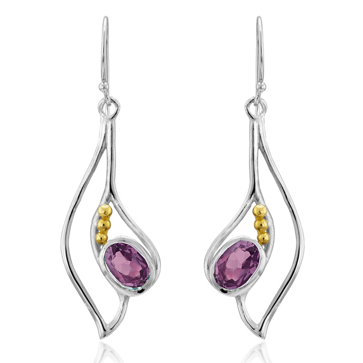 The Iris Earrings in various gemstones by Gallardo & Blaine Designs are a pair of silver & gold drop earrings featuring an organic, wavy design. Each earring has an oval-shaped purple gemstone set in the center and accented with three small gold beads on one side. These elegant gemstone earrings dangle from simple hooks.