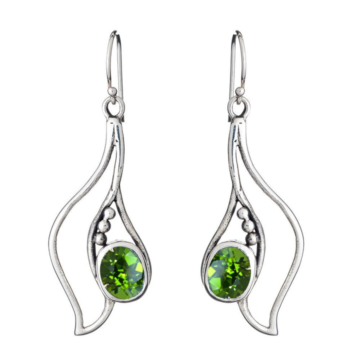 The Iris Earrings in various gemstones by Gallardo & Blaine Designs are a pair of silver dangling gemstone earrings with an artistic, flowing design. Each earring features three small silver beads and a single, oval-shaped green gemstone set in the center. The earrings have a fishhook backing.