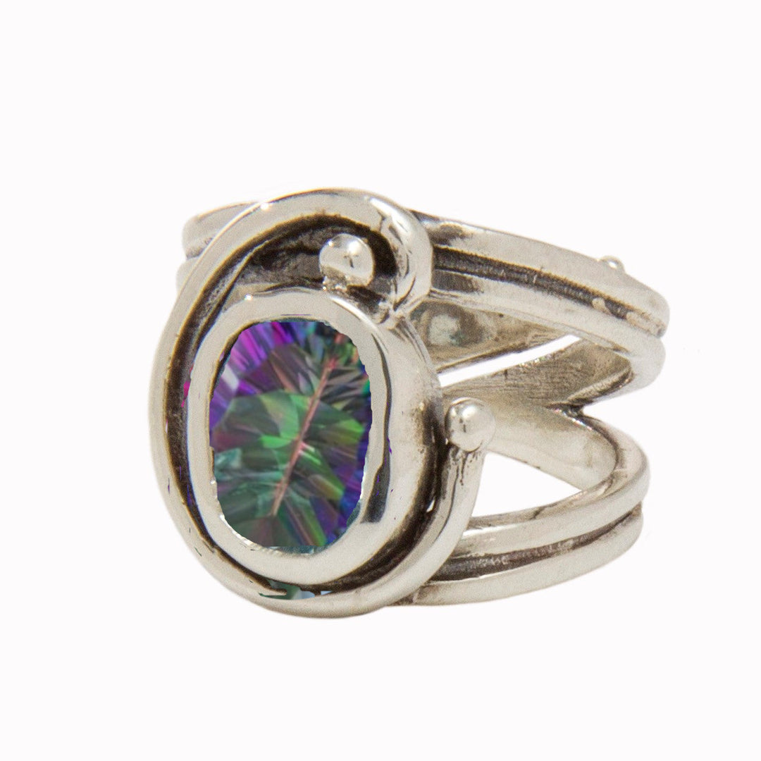 A stunning Art Nouveau ring featuring an abstract, swirled design with a prong setting that holds a large, oval-shaped, multicolored gemstone at its center. The gemstone displays a vivid, iridescent spectrum of teal, purple, and green hues. This exquisite piece is the Jasmine Ring in various gemstones by Gallardo & Blaine Designs.