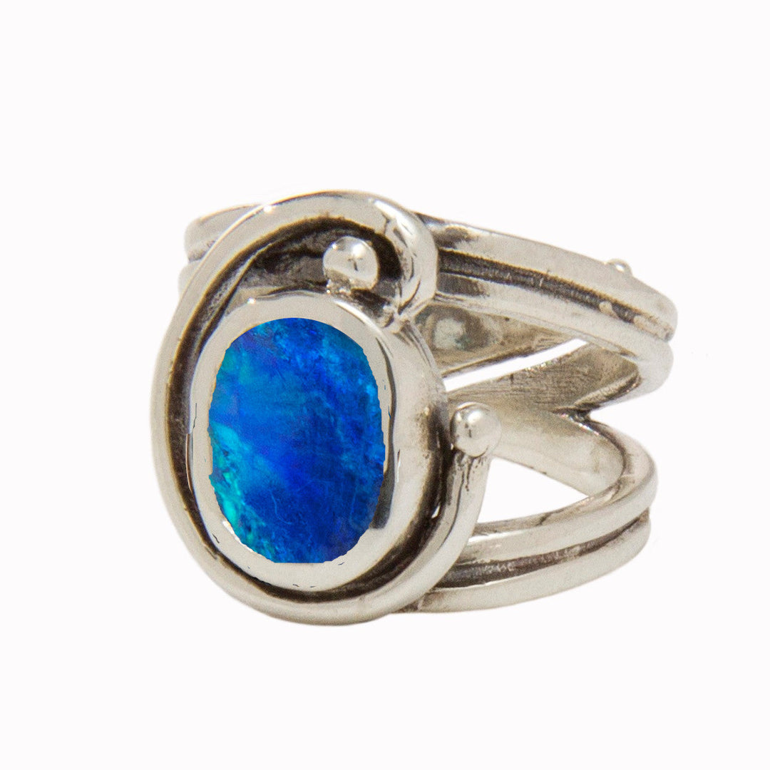 A Jasmine Ring in various gemstones by Gallardo & Blaine Designs featuring an intricate, swooping design which wraps around a vibrant oval blue gemstone at its center. The gemstones display tones of deep blue and lighter cyan, adding a striking contrast to the polished silver band.