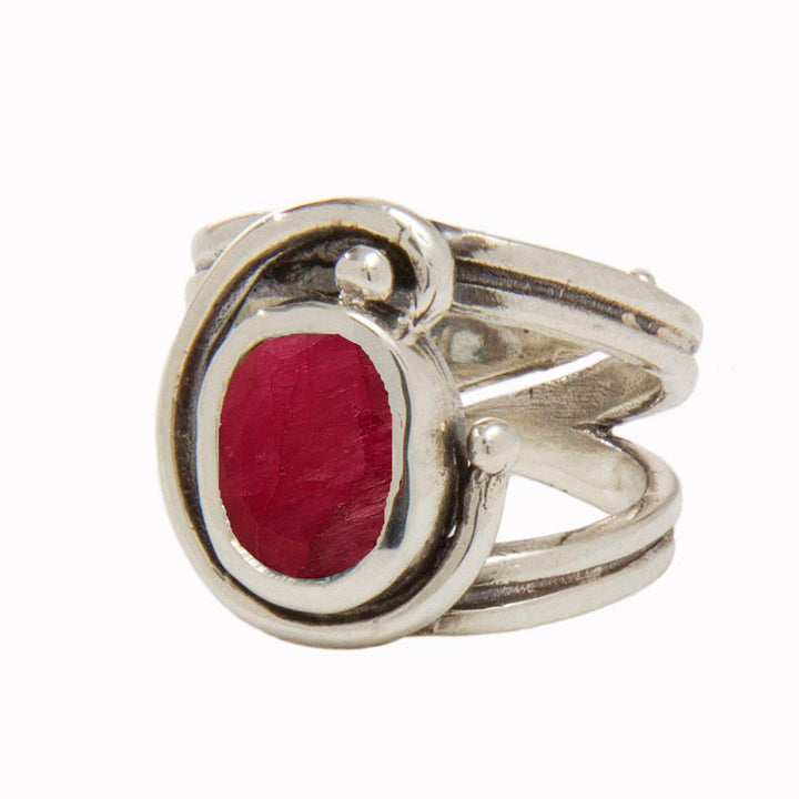 A silver Jasmine Ring in various gemstones by Gallardo & Blaine Designs featuring a large, oval-shaped red gemstone at its center. The band has a unique, intertwined design, giving it an elegant and intricate appearance. The ring appears to be polished, enhancing its shine against the plain white background.