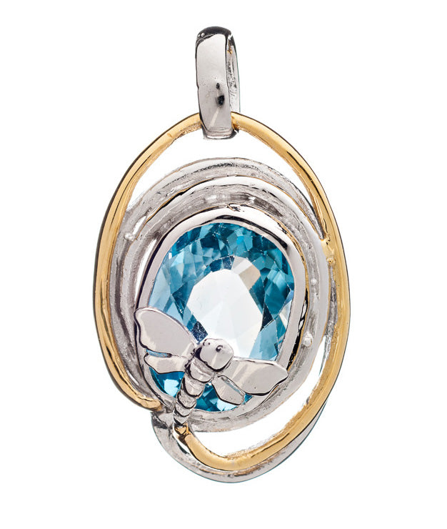 A Lagoon Pendant Small in various gemstones showcasing a large, faceted blue gemstone at its center by Gallardo & Blaine Designs. This unique piece features an intricate design with a small silver dragonfly perched on the gemstone, while the outer edge boasts a combination of delicate silver and gold loops encircling the dazzling stone.