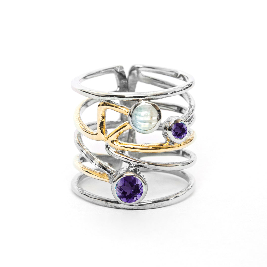 A stylish silver Lattice Ring in various gemstones by Gallardo & Blaine Designs featuring a contemporary, open band design with crisscrossing golden and silver bands. It is adorned with a blue moonstone and two purple gemstones, adding an elegant touch to its modern charm.