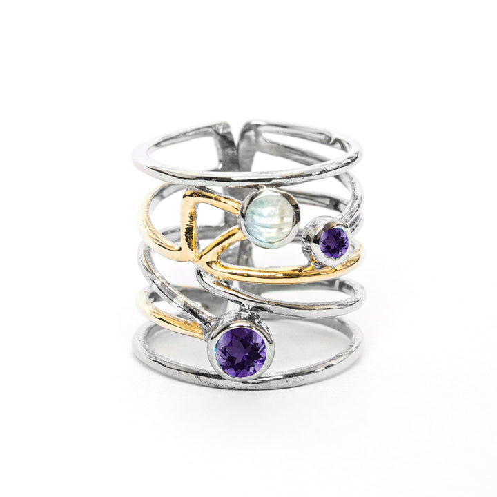 A stylish silver Lattice Ring in various gemstones by Gallardo & Blaine Designs featuring a contemporary, open band design with crisscrossing golden and silver bands. It is adorned with a blue moonstone and two purple gemstones, adding an elegant touch to its modern charm.