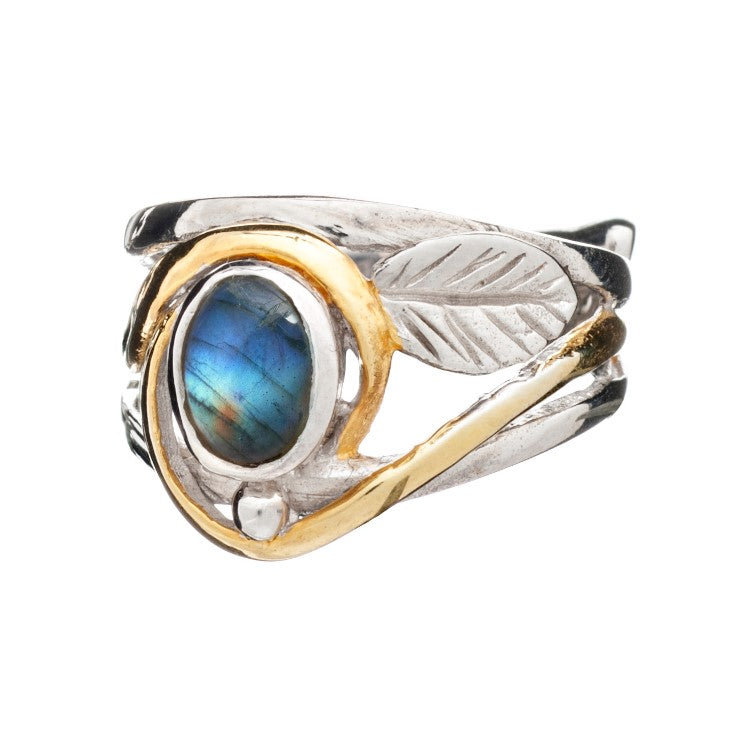 A ring featuring a central oval-shaped labradorite stone with a blue-green iridescence. The band combines silver & gold tones, designed with leaf-like engravings and an artistic, nature-inspired style. This elegant Leaf Ring in Silver Gold & various gemstones by Gallardo & Blaine Designs effortlessly captures the essence of natural beauty.