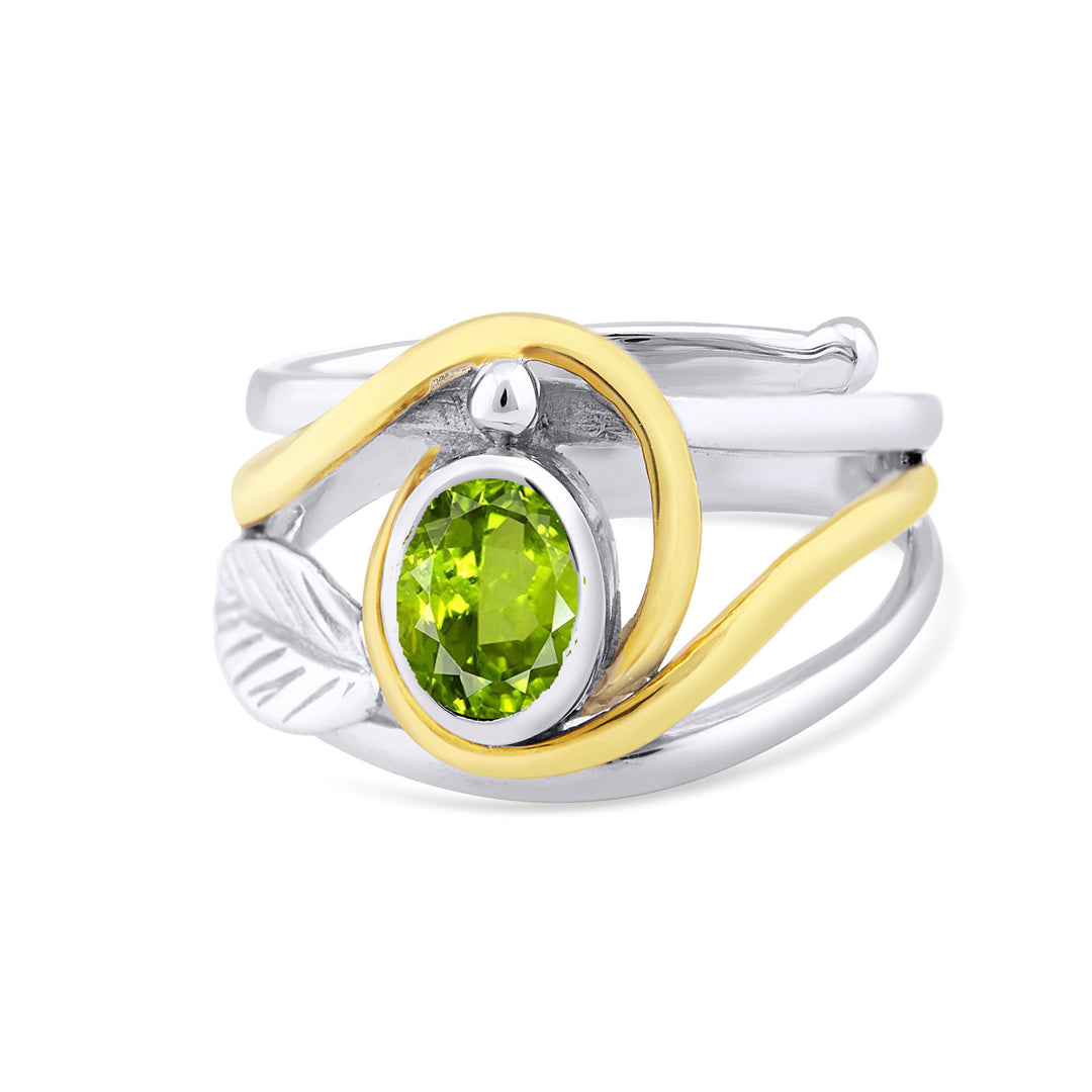 This elegant Leaf Ring in Silver Gold & various gemstones by Gallardo & Blaine Designs features a vivid green oval gemstone set in a two-tone band with a silver leaf accent on one side and a gold wave design wrapping around the stone. The band showcases an elegant, layered appearance, seamlessly blending silver & gold tones.