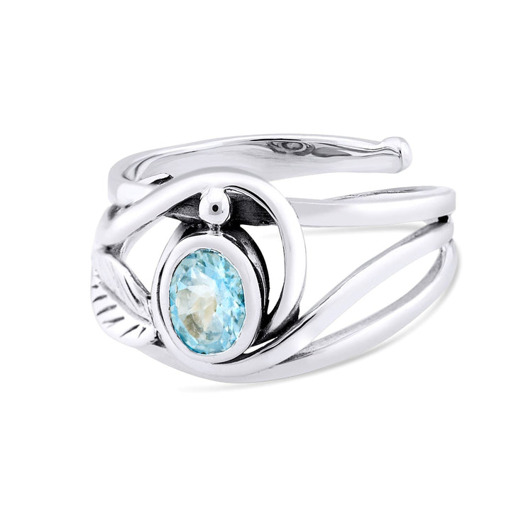 The Leaf Ring in Silver Gold & various gemstones by Gallardo & Blaine Designs is a stylish silver & gold ring featuring an elegant twisted design and a central oval blue gemstone. The band showcases flowing, intertwined curves with a smooth, shiny finish.