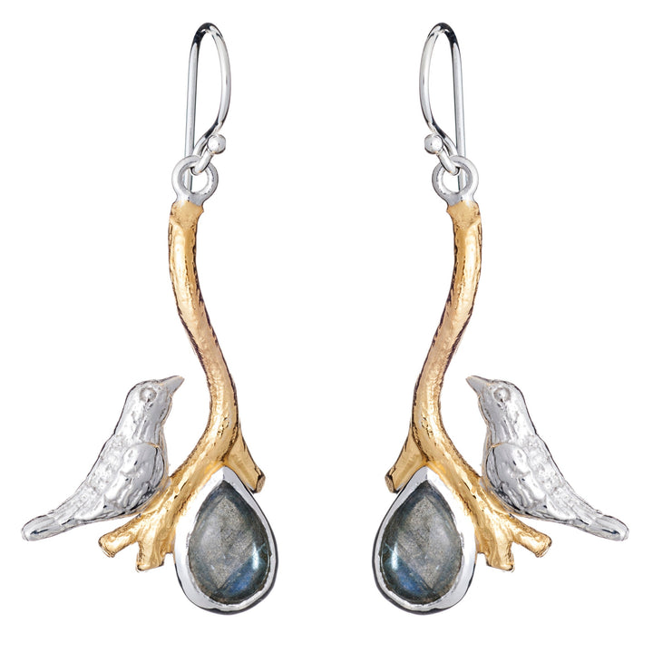 A pair of Lovebird Earrings in various gemstones featuring silver birds perched on golden branches. Below each bird hangs a teardrop-shaped pendant with a dark, reflective gemstone. These Gallardo & Blaine Designs dangle drop earrings have hook-style backings for wearing.