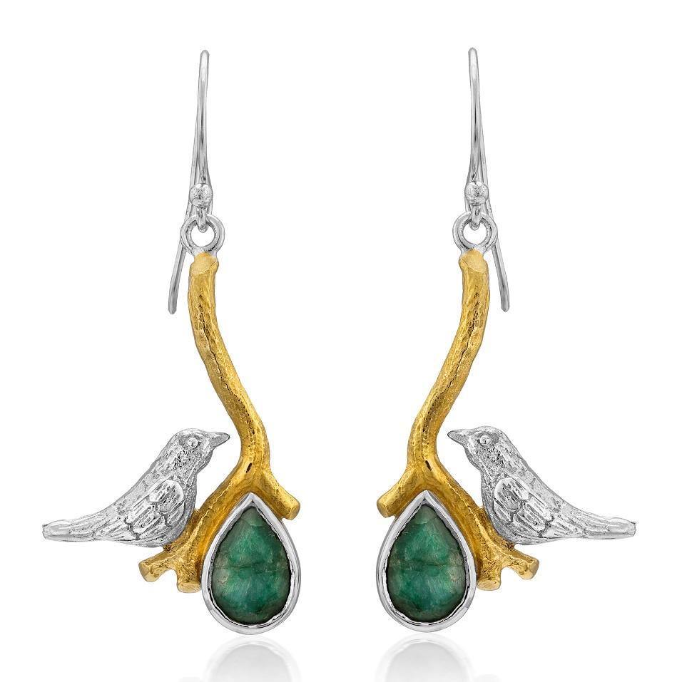 The Lovebird Earrings in various gemstones by Gallardo & Blaine Designs are a pair of elegant statement earrings featuring a small silver bird perched on a golden branch. Each branch extends down to hold a green teardrop-shaped gemstone. These dangle drop earrings hang gracefully from silver hooks, making them the perfect accessory for any occasion.