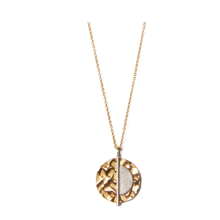 The Lunar Eclipse Pendant & Chain by Gallardo & Blaine Designs is a gold vermeil necklace featuring a textured round pendant on a delicate chain. The pendant design is split into two sections: one half is smooth sterling silver, while the other half boasts organic patterns. A vertical gold bar elegantly divides these two contrasting sections.