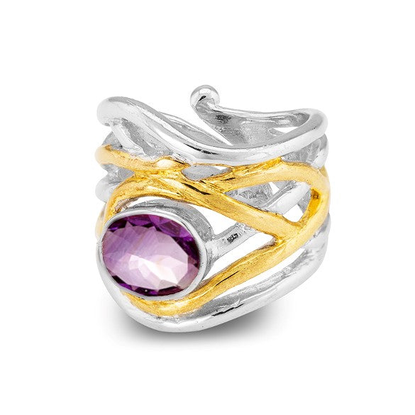 The Mayhem Ring in various gemstones by Gallardo & Blaine Designs with an intricate wavy design features a prominent gold accent wrapped around the band. The adjustable silver ring is set with a large, round, faceted purple gemstone in the center. The overall design is modern and artistic yet subtly medieval-inspired.