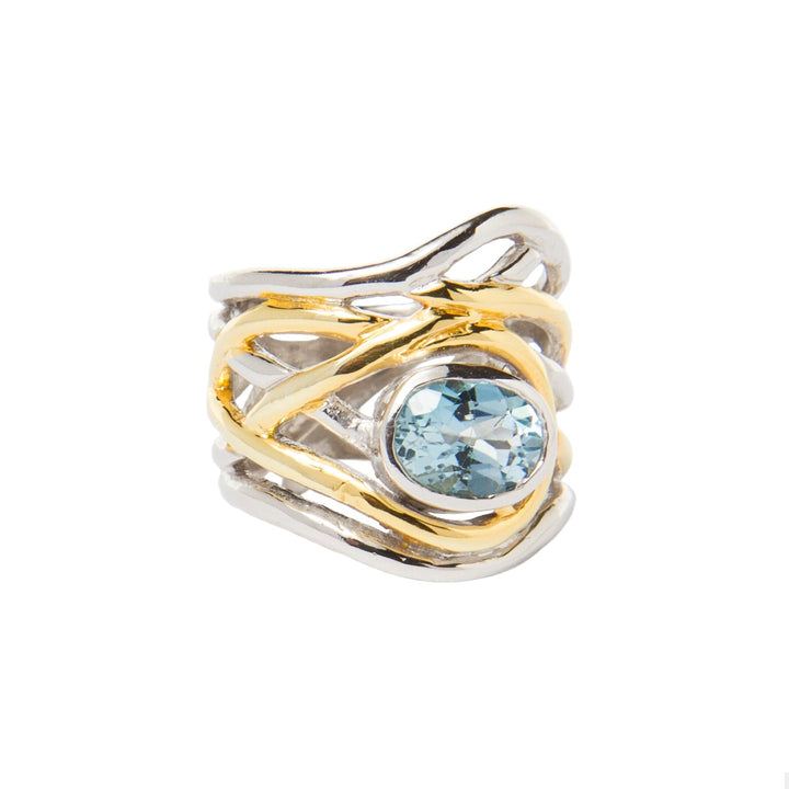 Introducing the Mayhem Ring in various gemstones by Gallardo & Blaine Designs: a silver and gold adjustable ring featuring an intricate, intertwined design with a central, round blue gemstone. The bands have an organic, wavy pattern, blending both metal colors harmoniously. This chunky statement ring exudes a touch of medieval-inspired jewelry elegance.