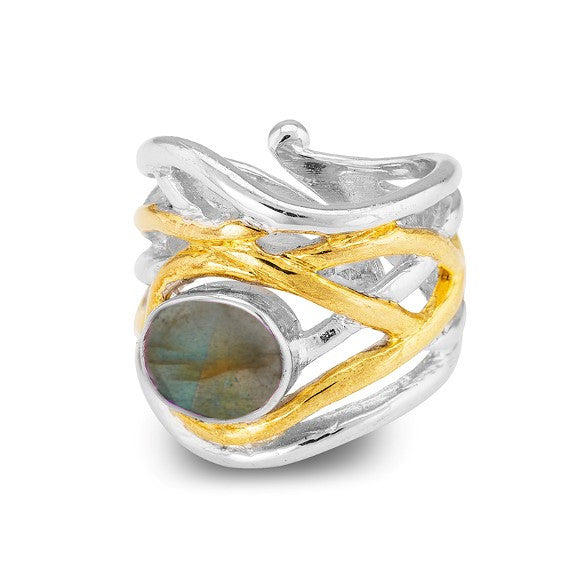 A chunky statement ring with an intricate design featuring intertwined silver and gold bands, crowned with a round, iridescent labradorite gemstone. The Mayhem Ring in various gemstones by Gallardo & Blaine Designs displays a range of colors when viewed from different angles, adding to the ring's elegant look.