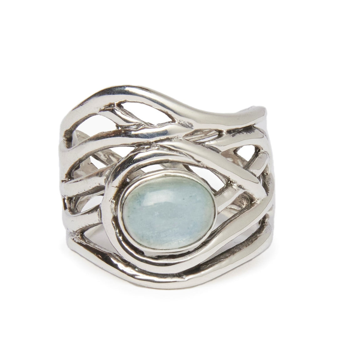 The Gallardo & Blaine Designs' Mayhem Ring in various gemstones features an intricate, flowing design that encapsules a smooth, light blue gemstone at its center. The openwork metal curves create an organic, wave-like pattern around the stone, offering a medieval-inspired jewelry vibe with its timeless elegance.