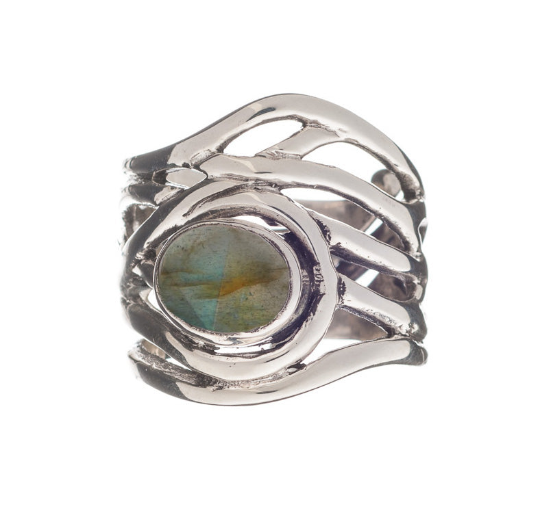 The Mayhem Ring in various gemstones by Gallardo & Blaine Designs features an intricate, wavy band design holding a central round labradorite gemstone with a blue-green iridescent hue. This adjustable ring has a modern, artistic appearance that brings a touch of medieval-inspired jewelry to its design.