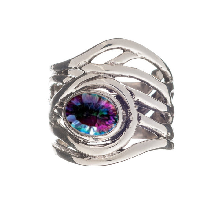 A chunky statement ring with a silver, overlapping band design holds a central gemstone that has a vibrant, multicolored pattern resembling an eye. This medieval-inspired jewelry piece is both bold and intricate. The Mayhem Ring in various gemstones by Gallardo & Blaine Designs perfectly exemplifies this unique aesthetic.