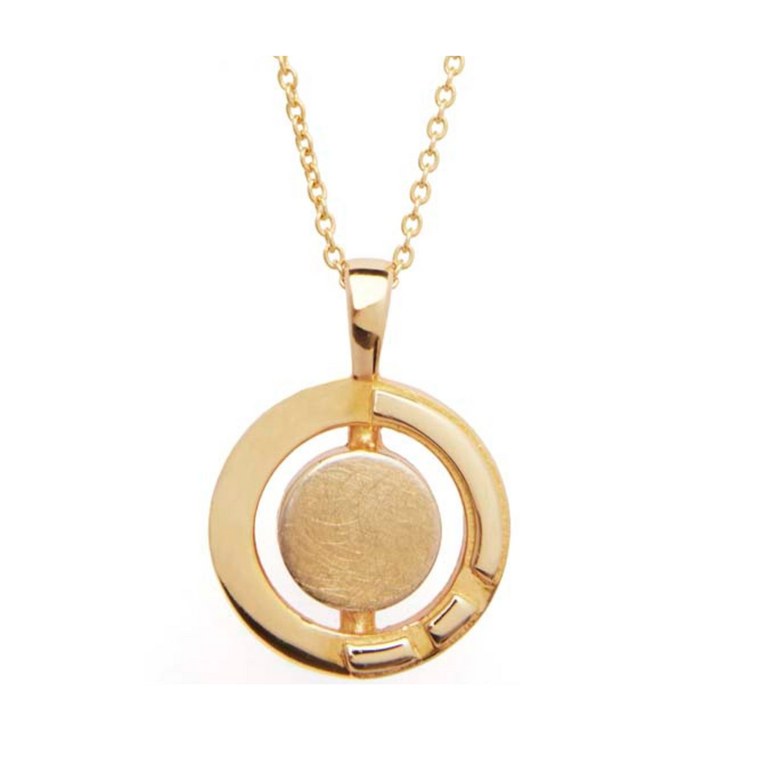 The Urú Large Pendant & Chain by Gallardo & Blaine Designs is a delicate gold pendant necklace featuring a circular design. The pendant has a smooth, round center encircled by a donut-shaped gold border with cut-out sections and three small, rectangular accents near the bottom. Inspired by Irish heritage jewelry, the chain is made of small interlinked loops.