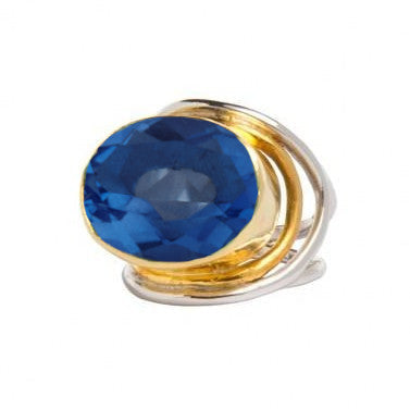 A Party Ring in various gemstones by Gallardo & Blaine Designs featuring a large, oval-shaped blue gemstone. The statement gemstone is set in a gold bezel with sterling silver bands artistically wrapping around it, creating an elegant and vibrant accessory.