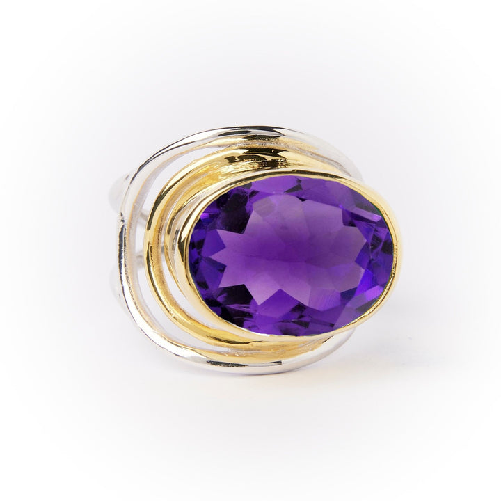 This Party Ring in various gemstones by Gallardo & Blaine Designs features a large, round purple gem set in the center, surrounded by an intricate sterling silver and gold band design. The faceted gemstone enhances its shine and depth, while the adjustable ring combines both metallic colors in a modern, artistic style.