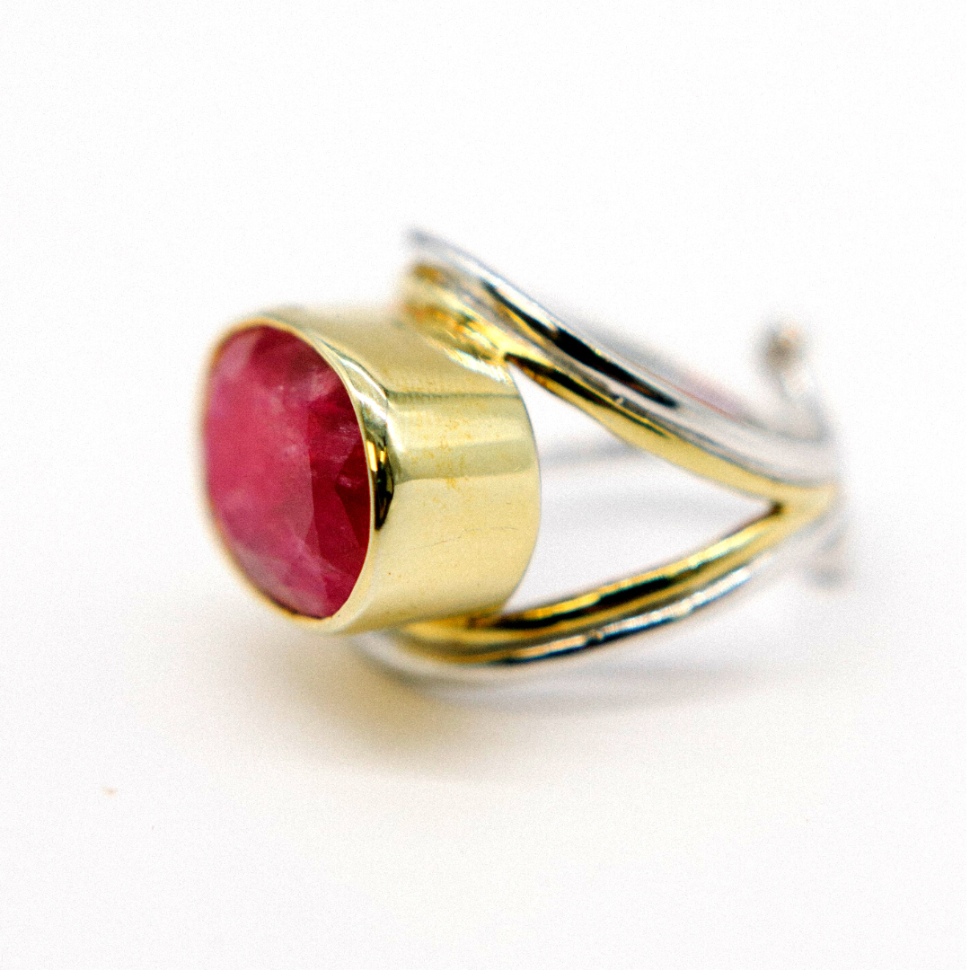 A close-up of the Gallardo & Blaine Designs Party Ring in various gemstones featuring a large, polished red gemstone set in a gold bezel. The adjustable band has an intricate design with intertwined sterling silver and gold elements, creating a sophisticated and elegant look. The white background highlights the ring's details.