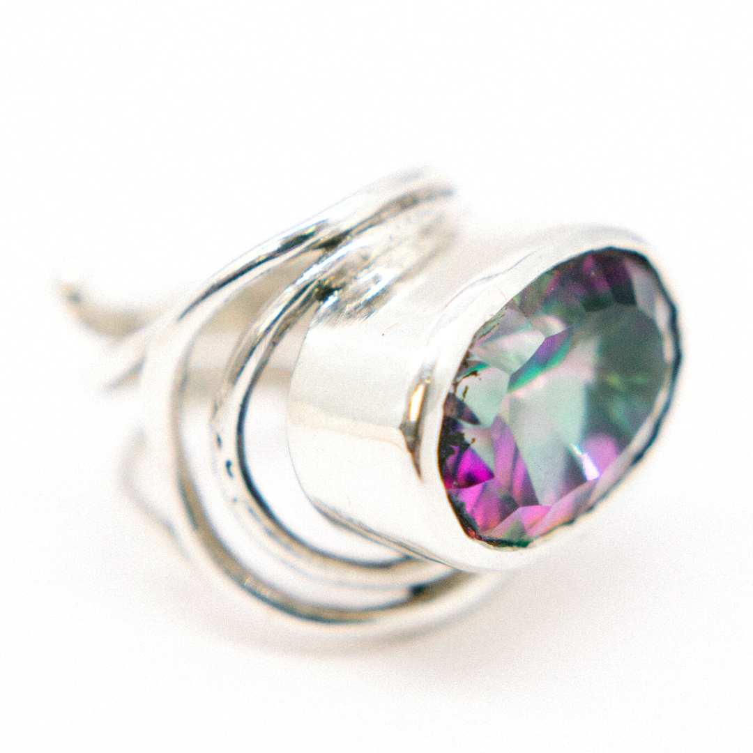 Close-up of a sterling silver & gold statement Gallardo & Blaine Designs Party Ring in various gemstones featuring a large, multi-colored gem. The stone exhibits shades of purple and green, with a faceted cut that catches the light. The band is elegantly twisted, adding a unique design element. The background is pure white.