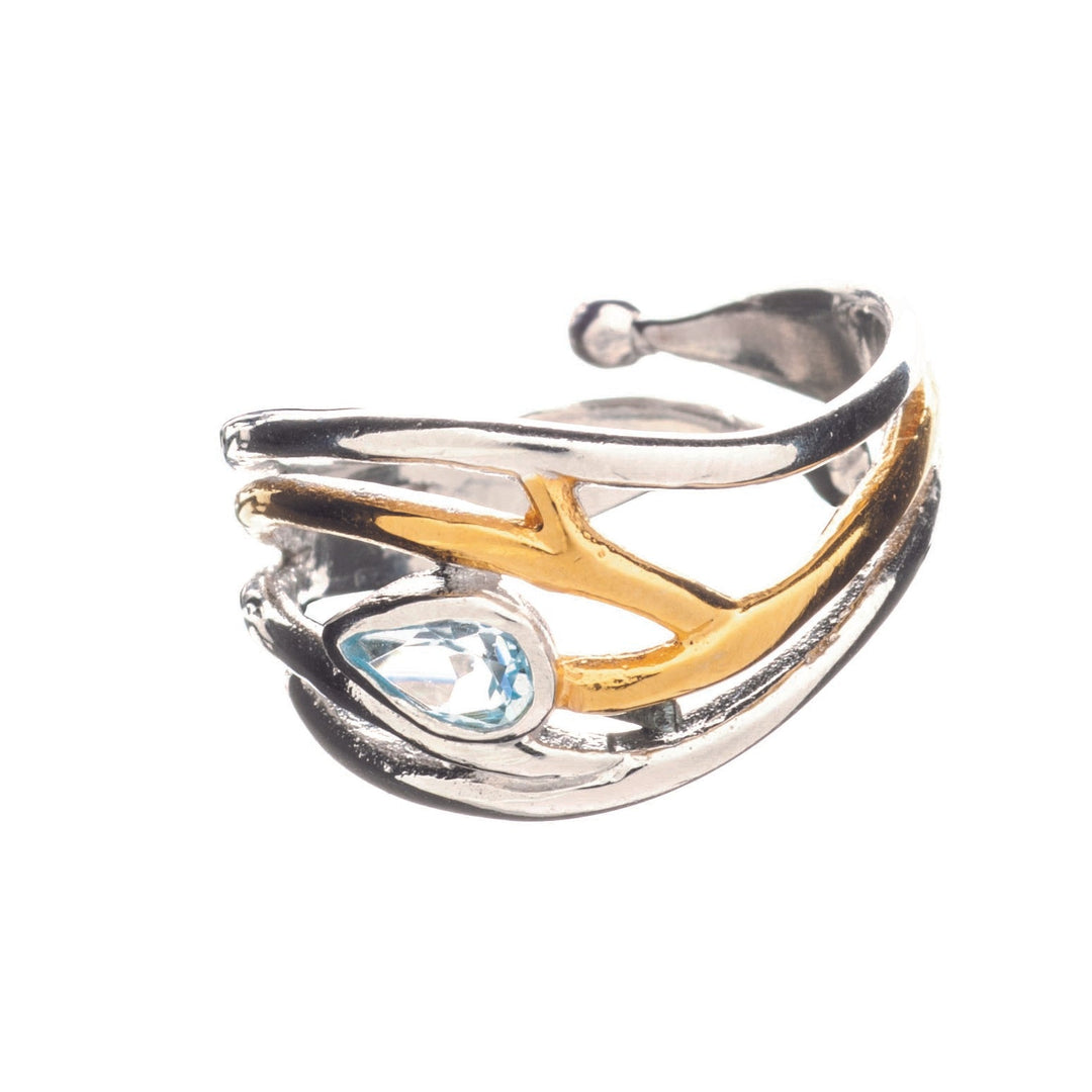 A silver and gold-toned Peacock Ring with an open design, featuring overlapping curves and branches. This elegant dainty ring showcases a teardrop-shaped blue gemstone set into one of the curves. The background is white, highlighting the ring's intricate details and mixed metals, adjustable in silver & gold. Introducing the Peacock Ring in various gemstones by Gallardo & Blaine Designs.