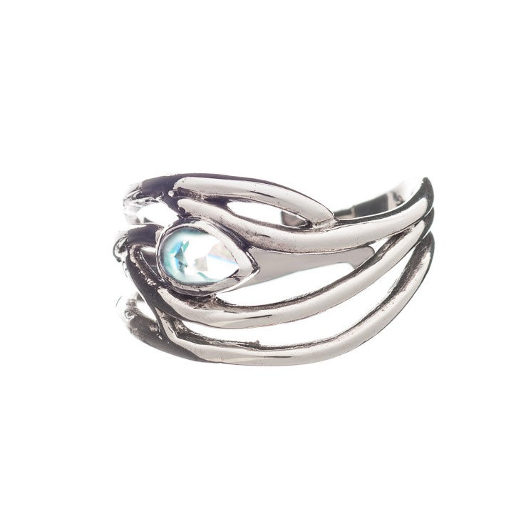 A silver Peacock Ring in various gemstones with an intricate, sculptural design features a central, teardrop-shaped light blue gemstone. The metalwork has a flowing, organic aesthetic, clasping the gemstone securely. This elegant dainty ring by Gallardo & Blaine Designs is displayed against a plain, white background.