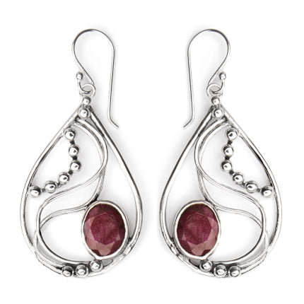 A pair of Gallardo & Blaine Designs Phoenix Earrings in various gemstones, teardrop-shaped and made of silver, featuring intricate swirling designs and small silver beads. Each earring boasts a large, oval, deep-red gemstone set at the base. These elegant drop earrings have hook fastenings at the top.