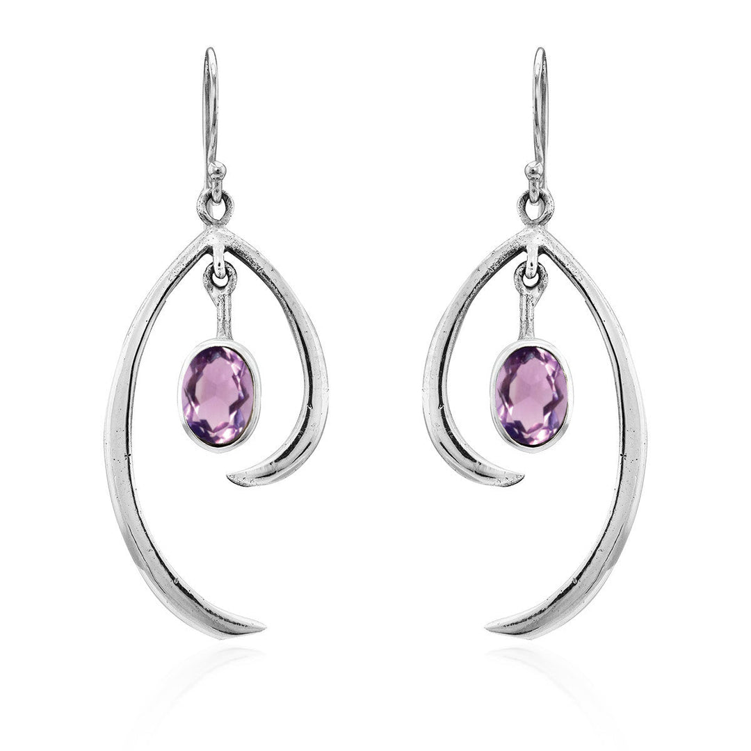 A pair of Gallardo & Blaine Designs Primrose Earrings in various gemstones featuring dangling oval-shaped purple gemstones. These sterling silver earrings include a sleek, curved metal element that elegantly cradles the gemstone, creating minimalist elegance with a simple yet stylish appearance.