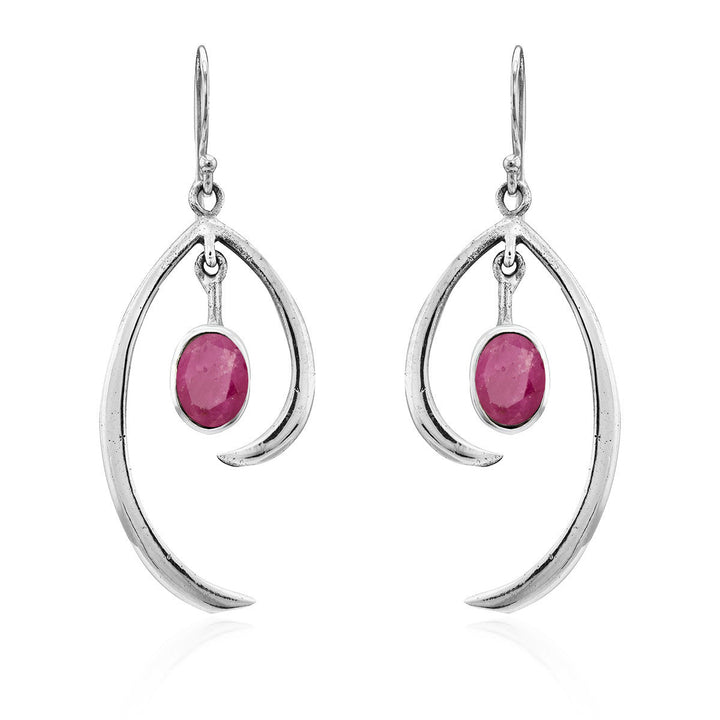 The Gallardo & Blaine Designs Primrose Earrings in various gemstones are a pair of sterling silver drop earrings featuring an elegant, curved design. Each earring showcases an oval-shaped pink gemstone hanging in the center. The minimalist elegance of the simple hooks adds to the delicate and refined aesthetic of this jewelry.