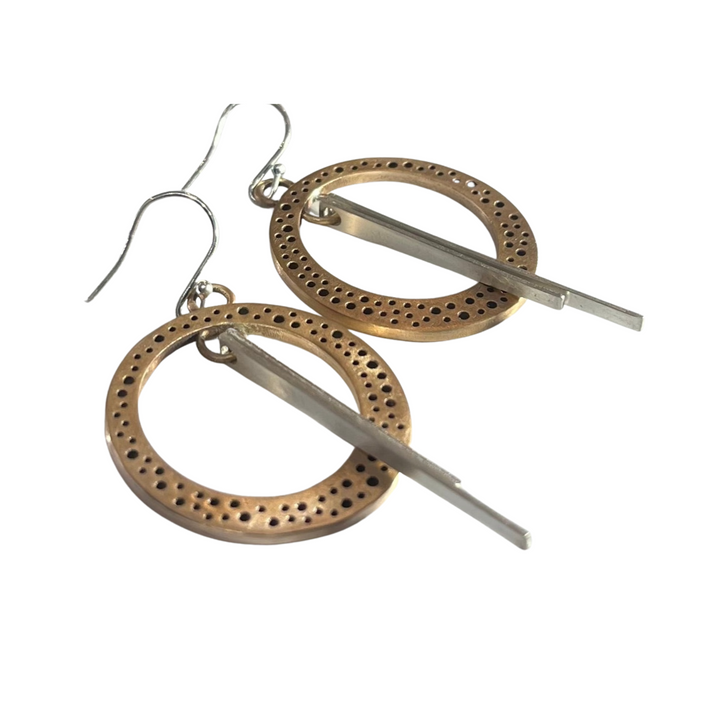 A pair of Rivera Earrings by Gallardo & Blaine Designs with intricate holes, reminiscent of Art Deco clockworks.