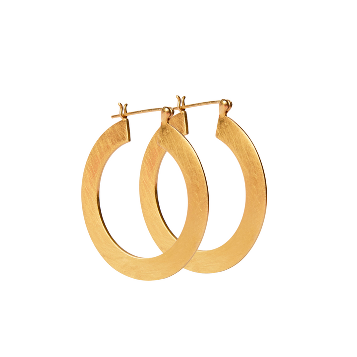 A pair of thin, gold vermeil Satin Hoop Earrings with a clasp fastening by Gallardo & Blaine Designs. The earrings have a smooth, polished finish and are suspended, showing their circular shape. The background is white, highlighting the shiny and elegant appearance of the earrings against the large flat surface.