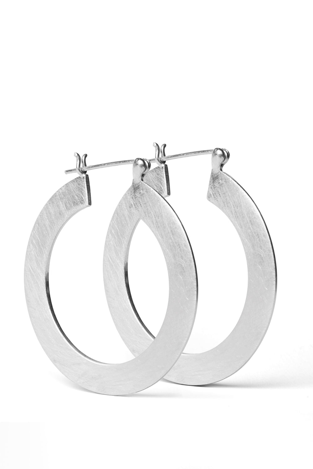 A pair of Satin Hoop Earrings by Gallardo & Blaine Designs with a large, flat matte finish is displayed against a white background. The earrings have a simple, elegant design and are shown slightly overlapping each other.