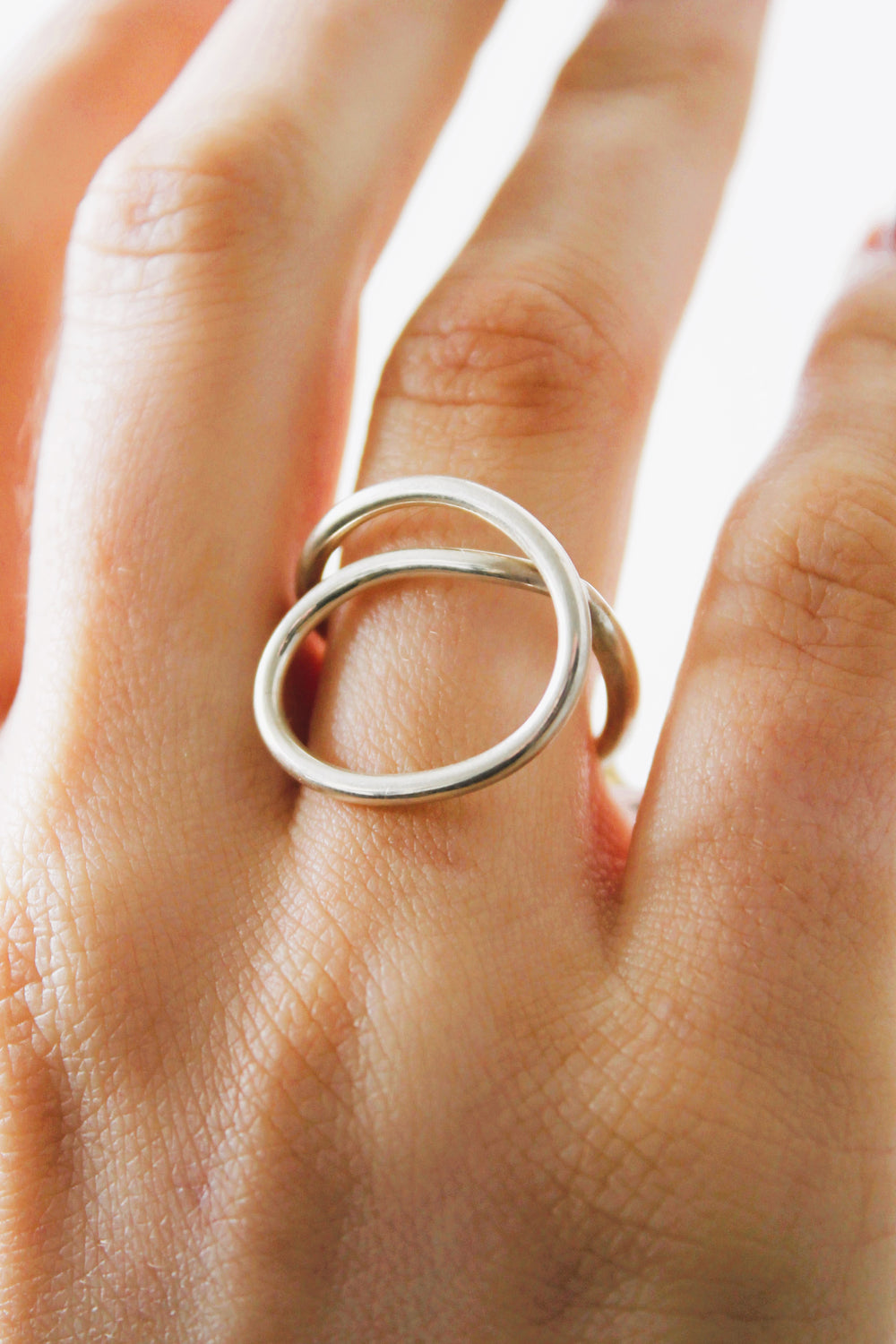 A close-up of a hand wearing the Sea Honey Ring by Gallardo & Blaine Designs, a minimalist sterling silver piece with two interlocking circles, shown against a soft light background.