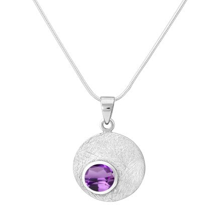 The Selene Necklace Silver - Small in various gemstones by Gallardo & Blaine Designs, crafted with a sterling silver chain, features a circular pendant. The pendant has a textured, silver surface and is adorned with a prominent round purple gemstone at its center, set in an elegant gold bezel.