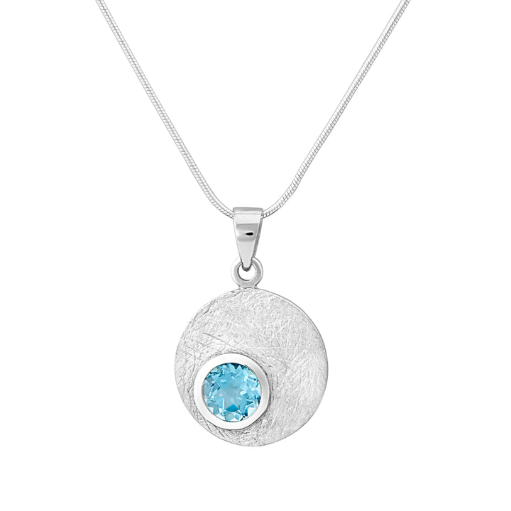 The Gallardo & Blaine Designs Selene Necklace Silver - Small in various gemstones showcases a textured circular pendant with a captivating blue gemstone at its core, elegantly framed by a gold bezel. It hangs gracefully from a thin sterling silver chain.