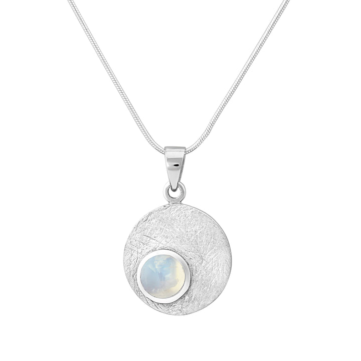 The Selene Necklace Silver - Small in various gemstones by Gallardo & Blaine Designs is a delicate piece featuring a round, textured pendant with a small moonstone at its center. The pendant is encased in a gold bezel and attached to a sleek Sterling silver chain, offering a minimalist yet elegant design.