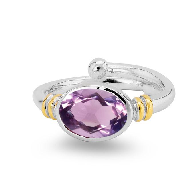 The Senna Ring in various gemstones by Gallardo & Blaine Designs is a silver adjustable ring featuring an oval cut purple gemstone in the center. The gemstone is held by a sleek, polished band with two small gold accents on each side. This elegant and modern design is perfect for anyone looking for a versatile and stylish gemstone ring.