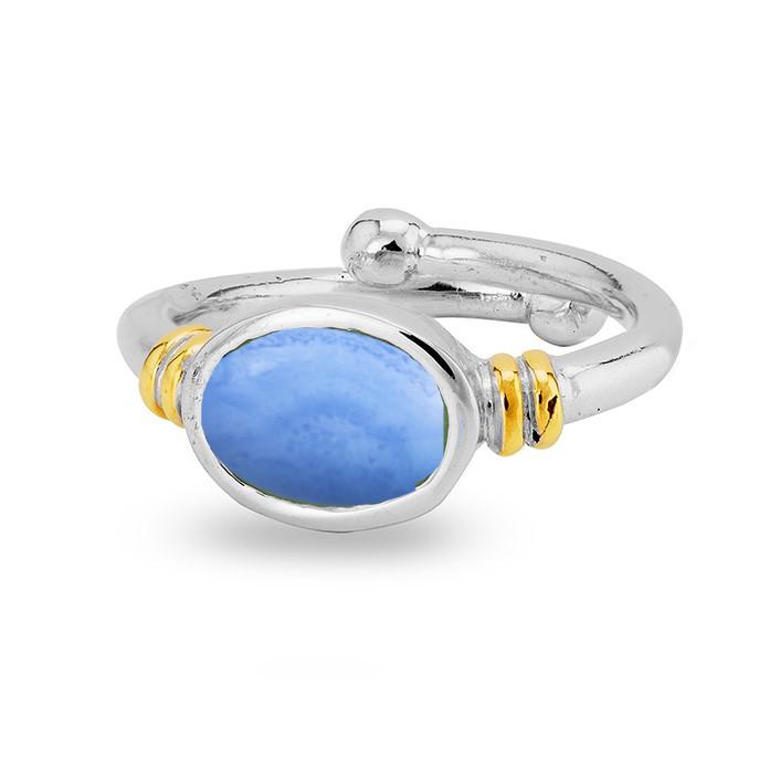 A silver, adjustable ring featuring a polished oval-shaped blue gemstone at its center. This Senna Ring in various gemstones by Gallardo & Blaine Designs includes gold-tone accents on either side of the gemstone, adding a touch of elegance to the overall design.