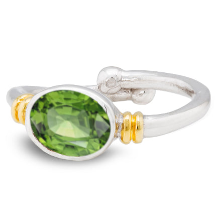 A Gallardo & Blaine Designs Senna Ring in various gemstones featuring an oval-shaped faceted green gemstone at its center. The gemstone is held by two gold accents on either side. The ring has a smooth, polished band that slightly overlaps at the back, making it an elegant and adjustable piece.