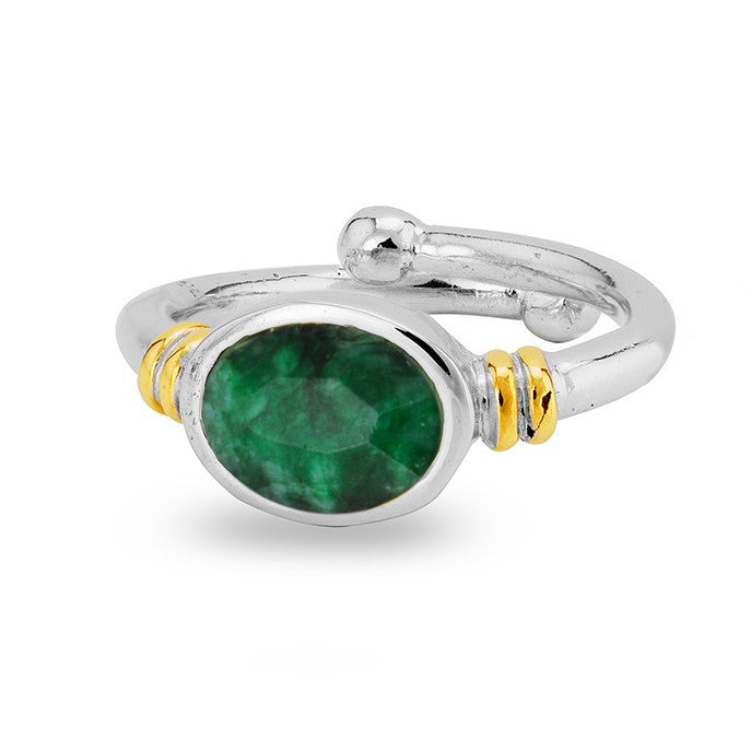 A Senna Ring in various gemstones by Gallardo & Blaine Designs featuring a green oval-shaped emerald gemstone set in the center. The ring has gold accents on either side of the stone, and a polished, smooth band with a decorative ball detail on top.