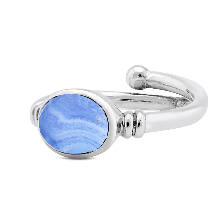 The Senna Ring in various gemstones by Gallardo & Blaine Designs features a polished silver gemstone ring with a large, oval-shaped blue stone adorned with white swirls. The band of the ring is smooth and splits near the setting, creating an open-ended design reminiscent of Art Nouveau style.