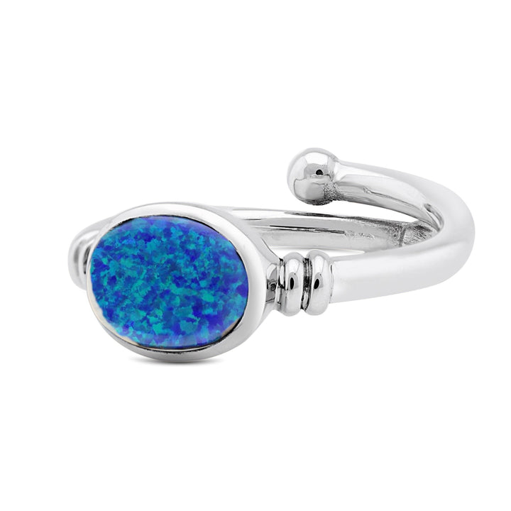 A Senna Ring in various gemstones with a large, oval-shaped blue opal stone set in the center from Gallardo & Blaine Designs. The opal exhibits a range of colors from deep blue to green, surrounded by a smooth, polished silver band with minimalist detailing, evoking the elegance of an Art Nouveau ring.